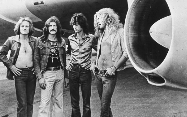 A black and white HD wallpaper featuring the band Led Zeppelin, with four members standing confidently near a large aircraft engine.