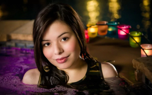 HD PC desktop wallpaper featuring celebrity Miranda Cosgrove smiling while partially submerged in water with colorful candles blurred in the background.