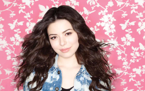 HD PC desktop wallpaper featuring celebrity Miranda Cosgrove posing against a pink floral background with long, flowing dark hair and a denim jacket.