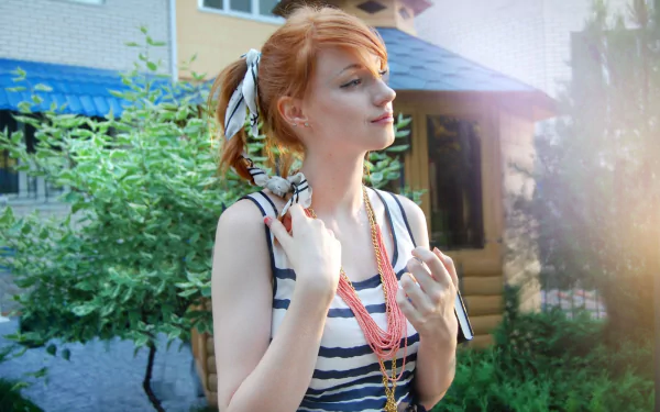 HD PC desktop wallpaper/background of a redheaded woman (tag withheld), striped top and layered necklaces, standing outdoors by greenery with sunlight and a house in the background.