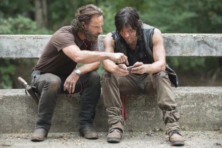 Rick Grimes (Andrew Lincoln) and Daryl Dixon (Norman Reedus) from The Walking Dead sit on a concrete ledge, engrossed in a conversation. This HD desktop wallpaper captures a moment from the TV Show.