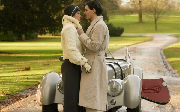 Period-romance scene: couple in 1930s attire embrace beside a vintage car on a leafy drive — 4K Ultra HD PC desktop wallpaper inspired by the film Easy Virtue.