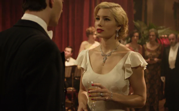 Blonde actress in a 1920s-style gown and necklace, holding a drink in an elegant ballroom — cinematic movie scene, 2K Quad HD PC desktop wallpaper/background.