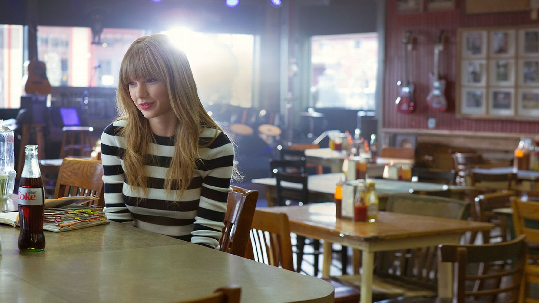 HD PC desktop wallpaper featuring Taylor Swift sitting alone in a cozy, softly lit café, blending music and serene ambiance.