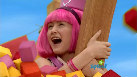 HD PC desktop wallpaper of a pink‑haired LazyTown character laughing among colorful foam blocks, hugging a wooden beam with a bright blue sky background.