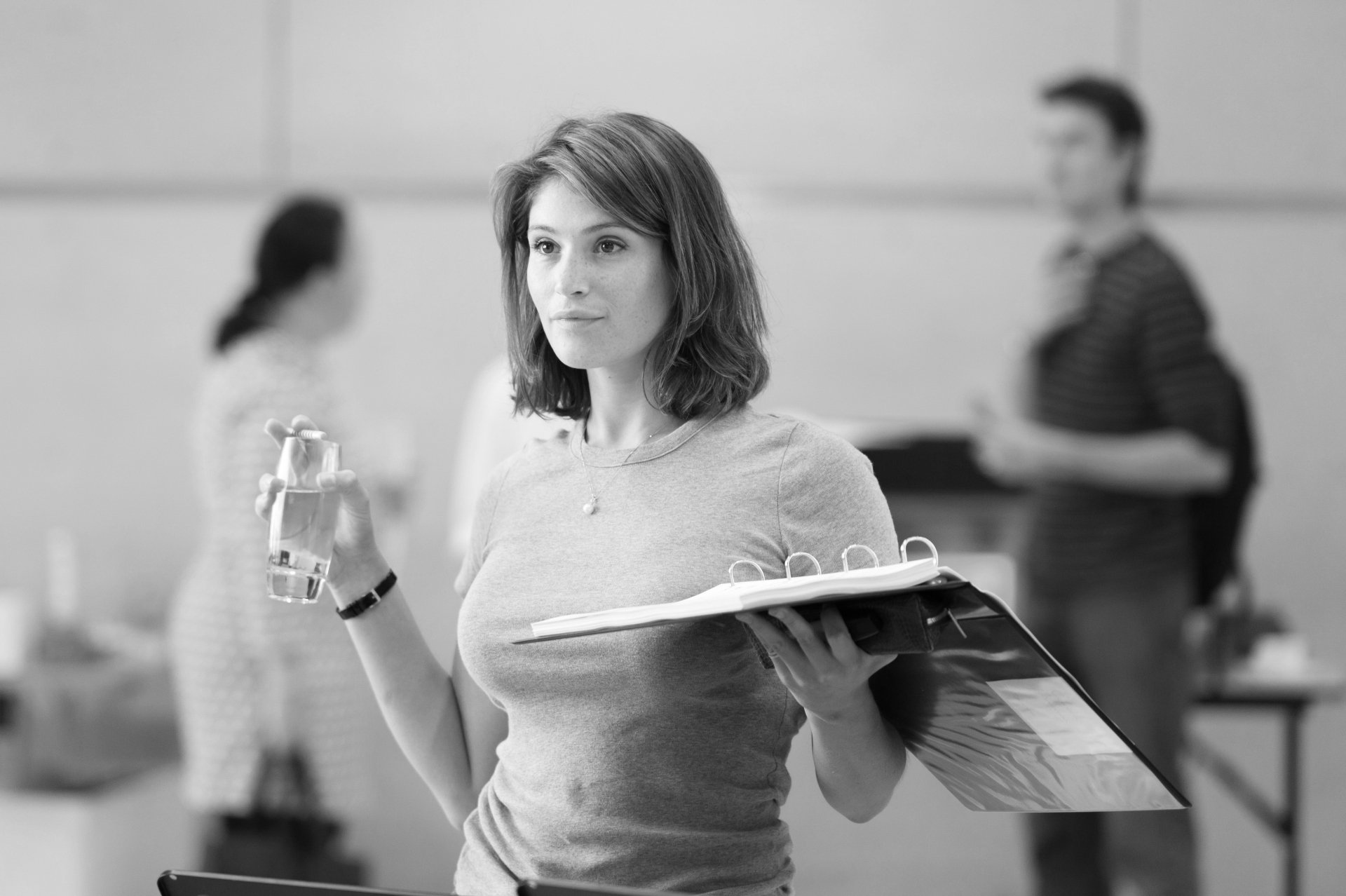 Black-and-white 4K Ultra HD wallpaper featuring Gemma Arterton from the movie Made in Dagenham, holding a binder and water bottle in a workplace setting.
