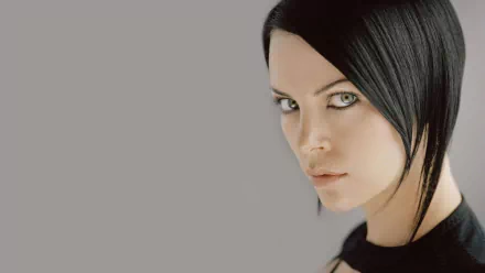 HD PC desktop wallpaper featuring Charlize Theron as Aeon Flux with a serious expression against a plain gray background.