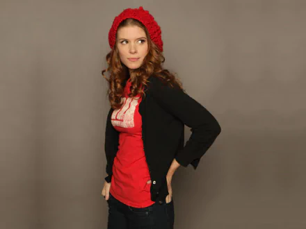 HD PC desktop wallpaper featuring celebrity Kate Mara wearing a red beanie and shirt with a black cardigan against a neutral background.