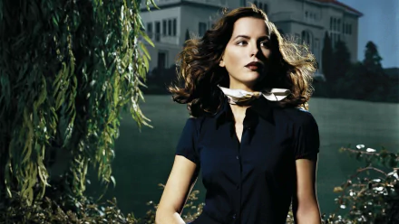 HD desktop wallpaper of Kate Beckinsale from the movie The Aviator, featuring her standing outdoors with flowing hair and a dark outfit against a lush background.