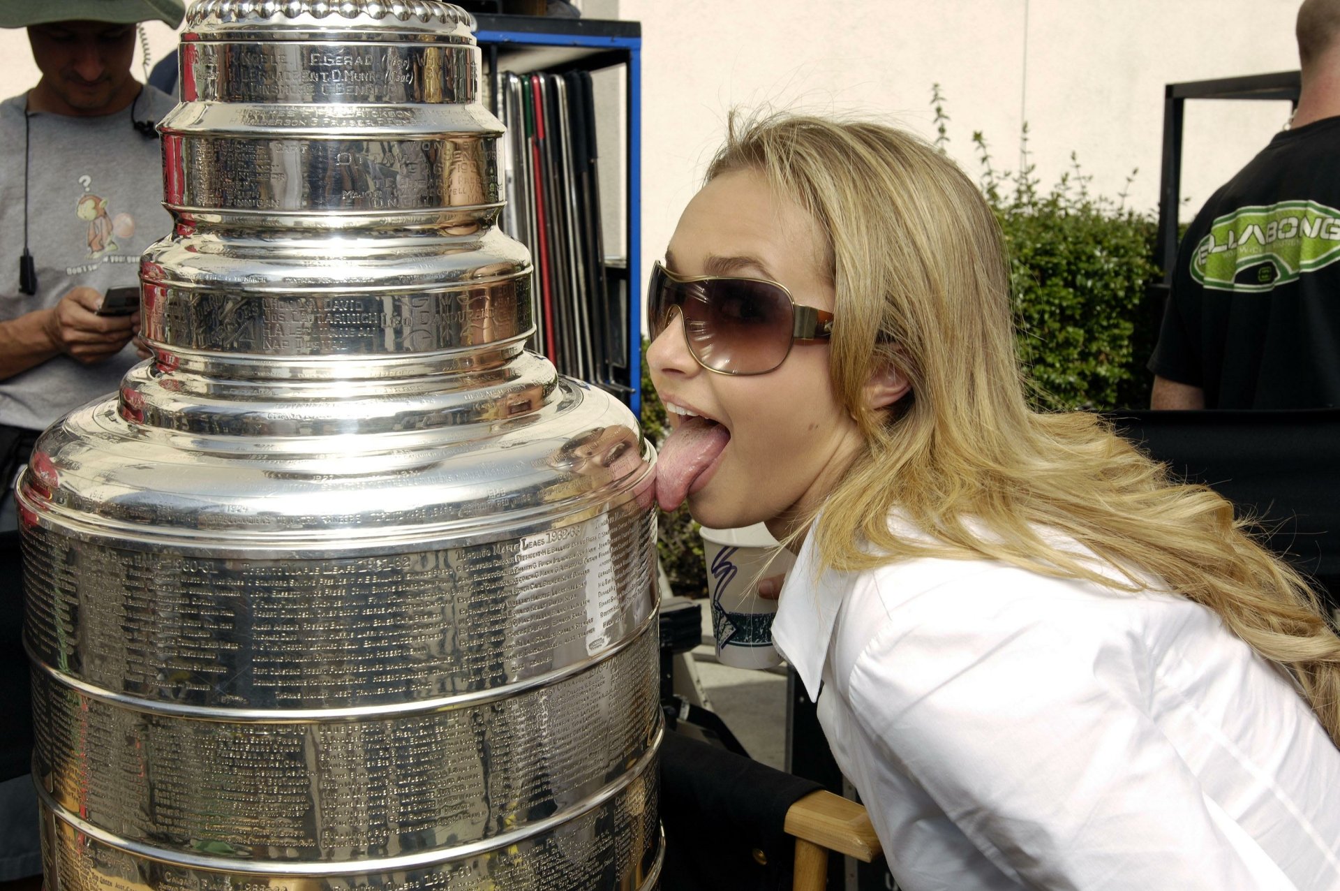 Person in sunglasses playfully licking a large silver hockey trophy outdoors — 2K Quad HD PC desktop wallpaper and background.