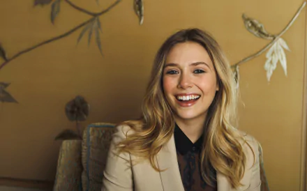 A smiling Elizabeth Olsen poses in a stylish outfit, set against a warm, decorative background, showcasing her charm in this high-definition desktop wallpaper.