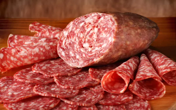 Close-up of sliced salami and a whole salami on a wooden board, vivid 2K Quad HD PC desktop wallpaper and background.
