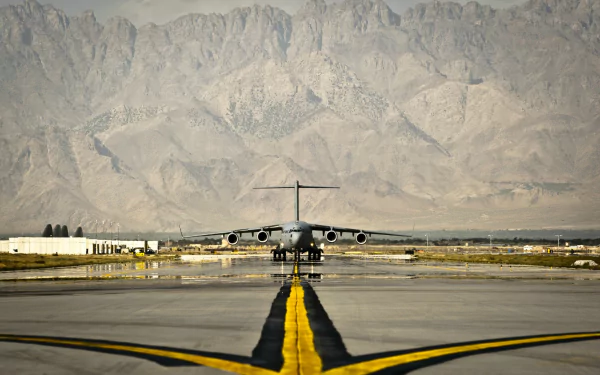 Military Boeing C-17 Globemaster III centered on a runway with rugged mountains behind — HD PC desktop wallpaper and background.
