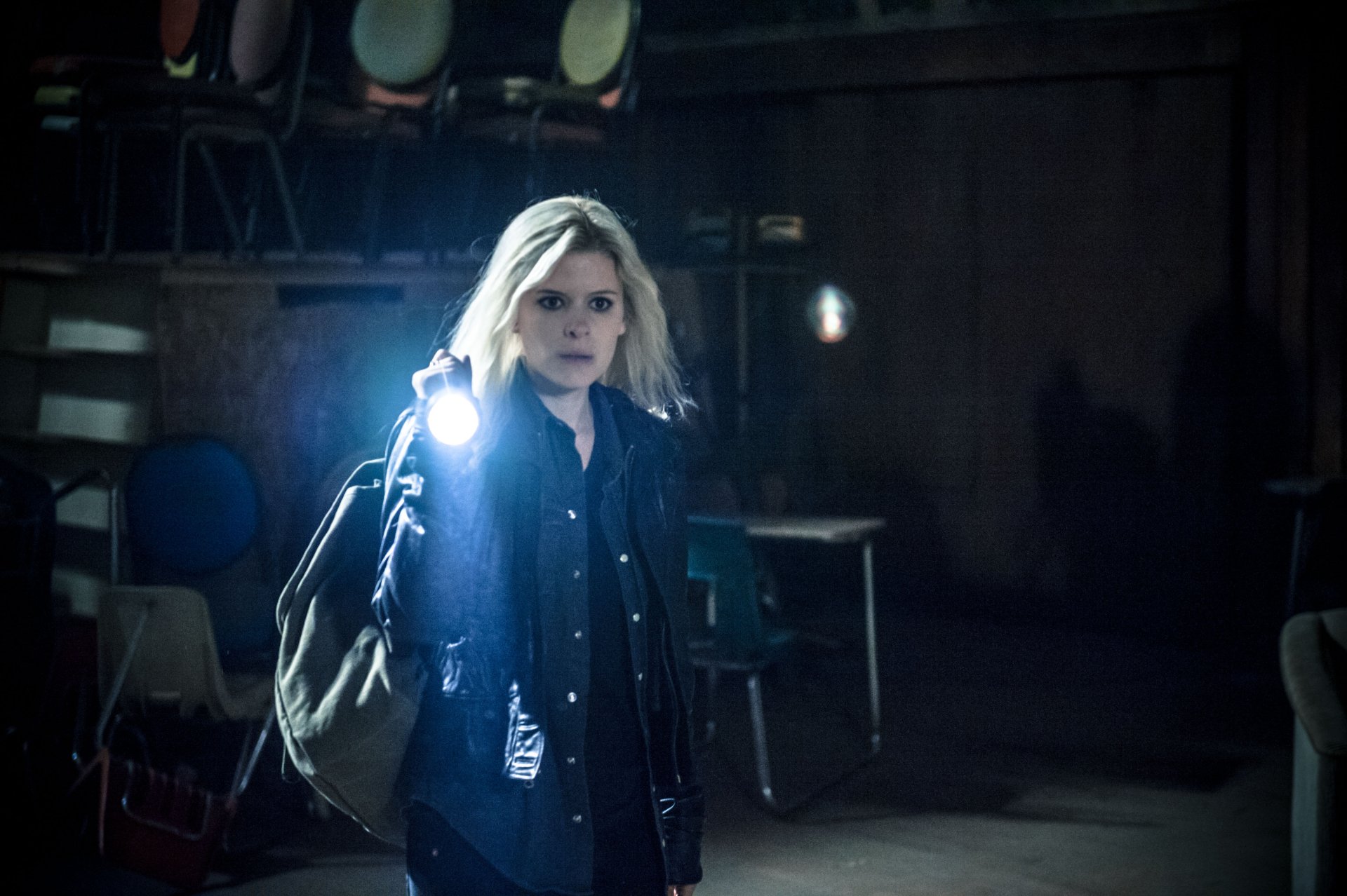 4K Ultra HD PC desktop wallpaper — dim movie still of a blonde woman holding a flashlight and shoulder bag, standing in a shadowy, empty room.