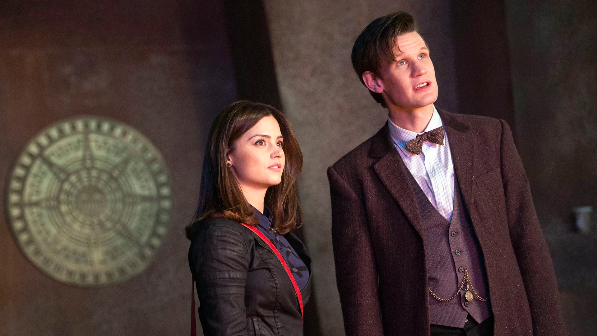 HD desktop wallpaper featuring Jenna Coleman and Matt Smith from the TV show Doctor Who (2005), standing against a dark background with a circular emblem.