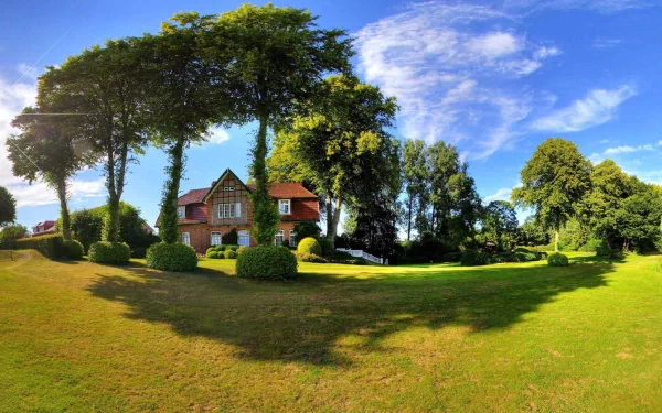HD desktop wallpaper of a charming house surrounded by lush green lawns, tall trees, and a vibrant blue sky.