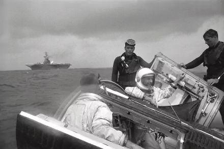 Black-and-white 2K desktop wallpaper of NASA Gemini 9 man-made space capsule recovery at sea: an astronaut in the hatch with crew assisting, aircraft carrier on the horizon.