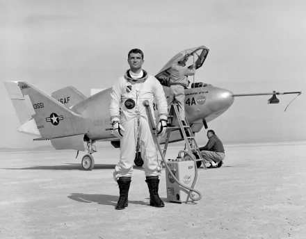 A NASA astronaut stands confidently in a flight suit next to the Martin Marietta X-24A aircraft, with crew members preparing for an upcoming test flight in the background.