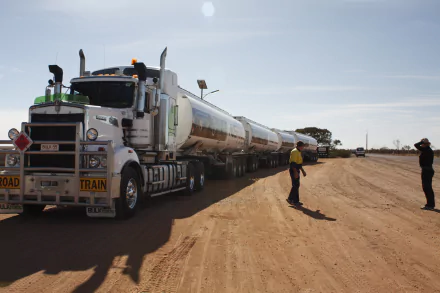 A Kenworth road train vehicle with multiple trailers parked on a dusty road under a clear sky, featured as a 4K Ultra HD PC desktop wallpaper.