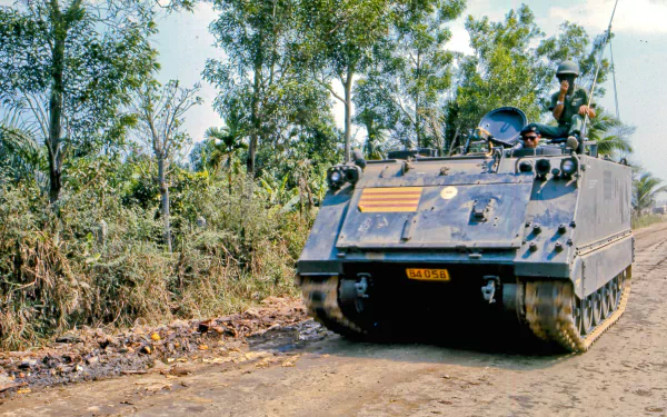 HD desktop wallpaper depicting a military armored vehicle navigating a dirt road surrounded by dense foliage during the Vietnam War.