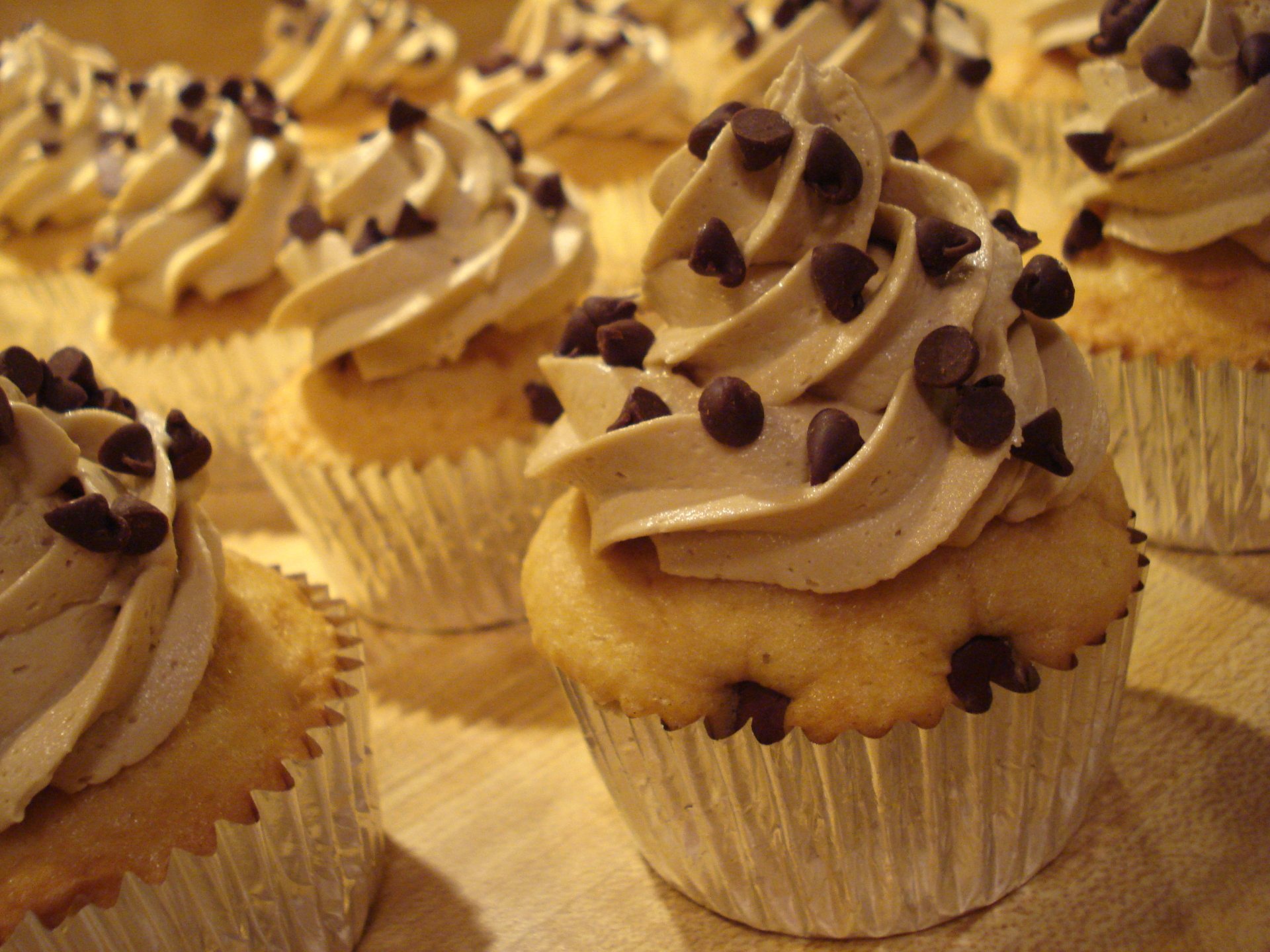 Close-up of chocolate-chip-topped cupcakes with swirled frosting, presented as a 2K Quad HD PC desktop wallpaper background.