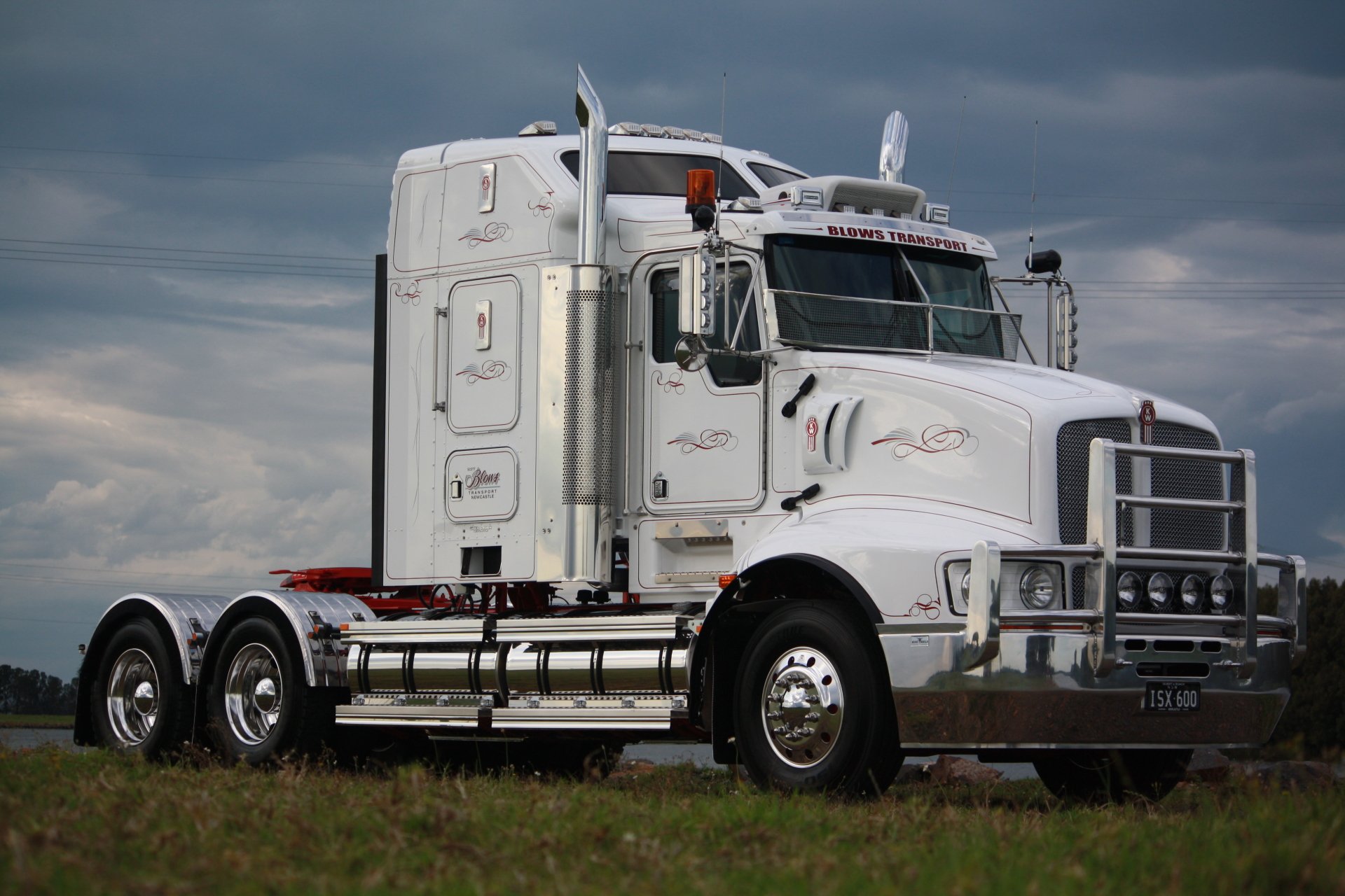White Kenworth semi truck parked on grass beneath dramatic clouds, 4K Ultra HD PC desktop wallpaper background of a vehicle.