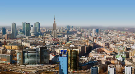 HD PC desktop wallpaper: panoramic man-made skyline of Warsaw featuring the Palace of Culture and Science and modern high-rises beneath a clear blue sky.