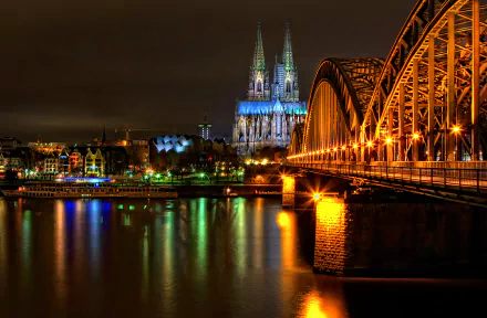 A stunning HD wallpaper featuring the illuminated Cologne Cathedral and Hohenzollern Bridge at night, showcasing the beauty of man-made structures along the river.