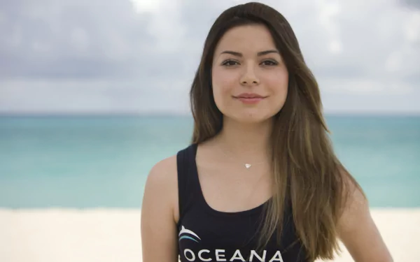HD PC desktop wallpaper featuring celebrity Miranda Cosgrove standing on a beach with the ocean and sky in the background.