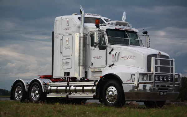 White Kenworth semi truck parked on grass beneath dramatic clouds, 4K Ultra HD PC desktop wallpaper background of a vehicle.