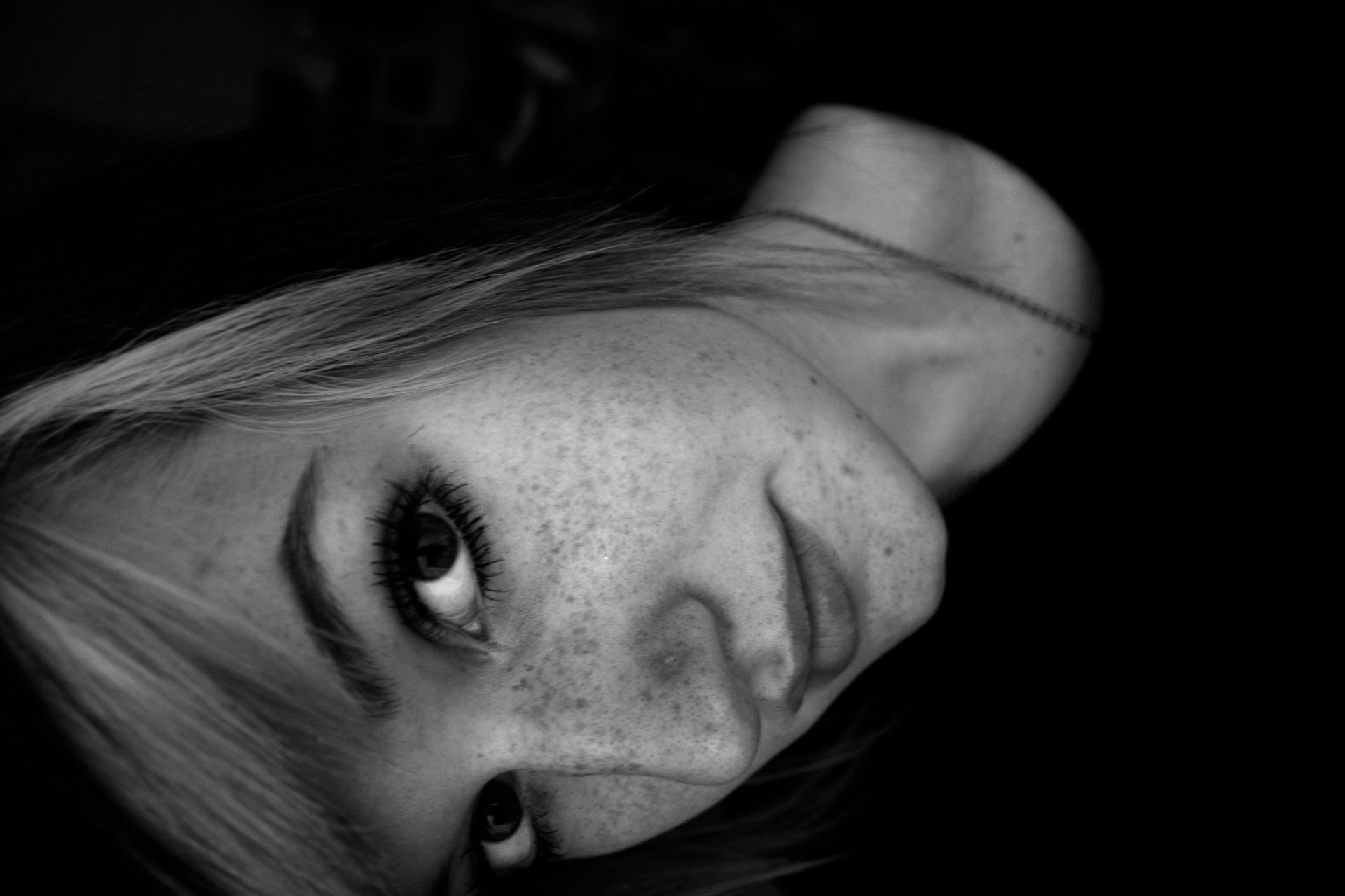 Black-and-white close-up of a freckled woman's face, tilted sideways with an intense gaze — 4K Ultra HD PC desktop wallpaper.