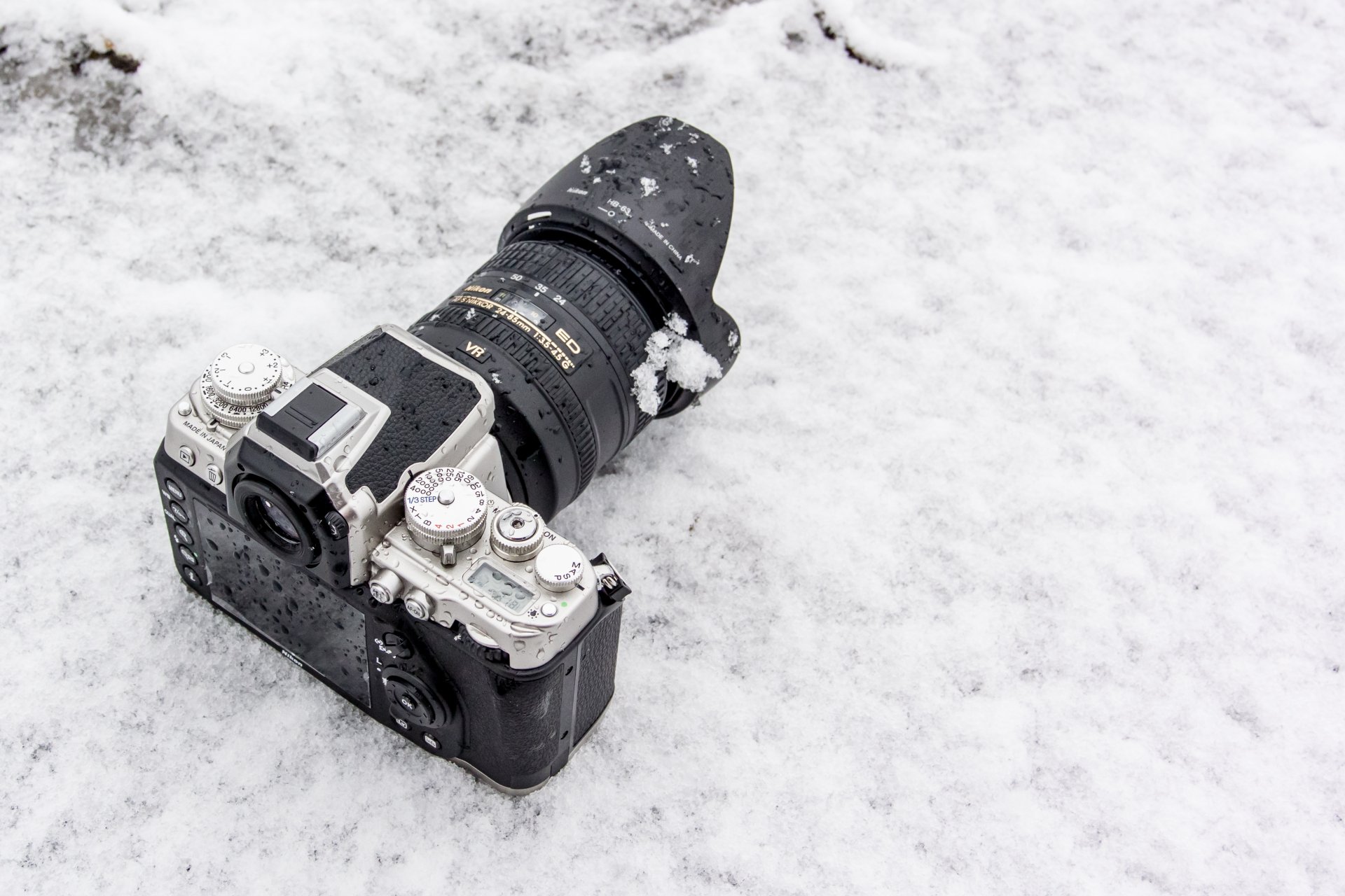 Snow-dusted Nikon camera lies on fresh snow — crisp man-made subject captured as a 4K Ultra HD PC desktop wallpaper and background.