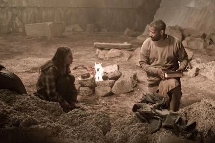 2K Quad HD PC desktop wallpaper: two actors — a man and woman — sit by a campfire in a dusty, ruined shelter in a gritty scene from the movie The Book of Eli.