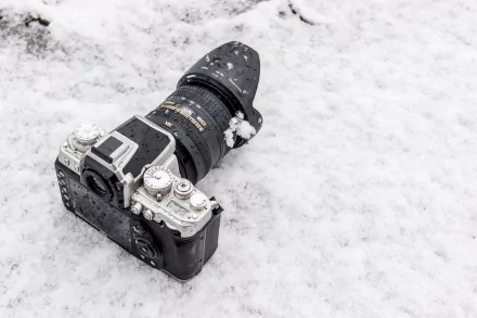 Snow-dusted Nikon camera lies on fresh snow — crisp man-made subject captured as a 4K Ultra HD PC desktop wallpaper and background.