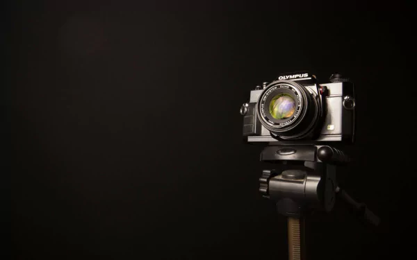 HD wallpaper showing a black Olympus man-made camera mounted on a tripod against a dark background.