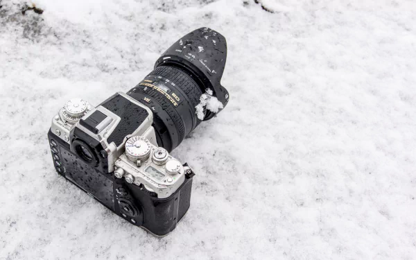 Snow-dusted Nikon camera lies on fresh snow — crisp man-made subject captured as a 4K Ultra HD PC desktop wallpaper and background.