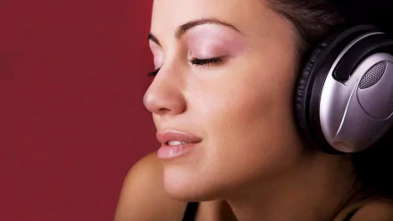 Close-up HD desktop wallpaper of a woman’s serene face with eyes closed, wearing headphones against a red background.