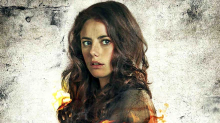 A dramatic still from Maze Runner: The Scorch Trials features Kaya Scodelario, showcasing her intense expression against a textured background with fire elements.