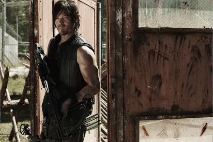 Daryl Dixon holding a crossbow in a scene from The Walking Dead. Played by Norman Reedus, he stands in an old, weathered doorway. HD desktop wallpaper and background.