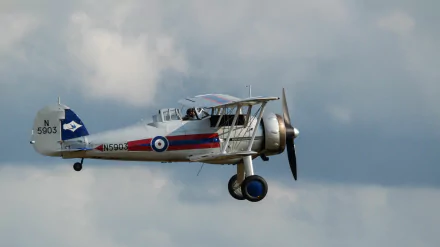 Military Gloster Gladiator biplane in flight against a cloudy sky — 5K Ultra HD PC desktop wallpaper/background.