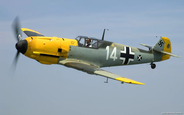 An HD desktop wallpaper featuring a Messerschmitt Bf 109 in flight, showcasing its distinct yellow and green camouflage and military insignia.
