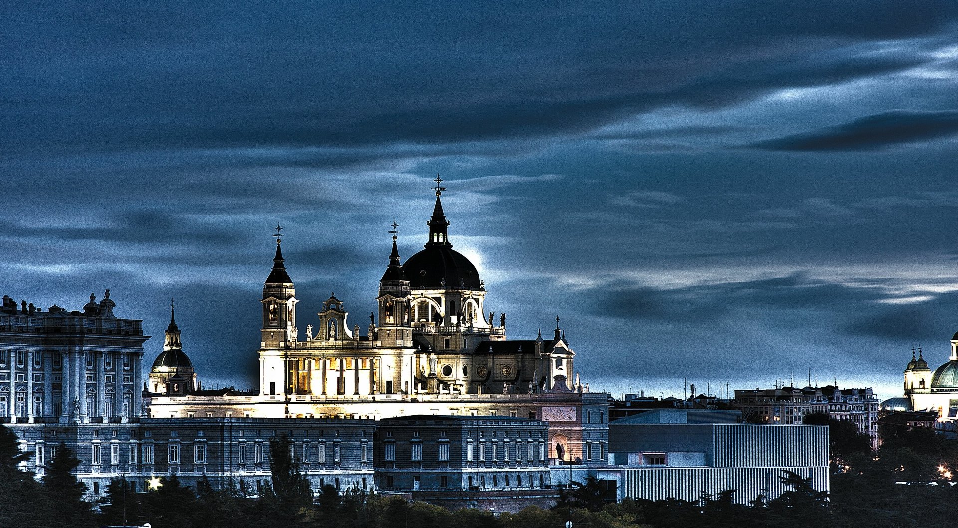 Night view of Madrid's Almudena Cathedral illuminated against a dramatic sky — religious landmark rendered as a 2K Quad HD PC desktop wallpaper and background.