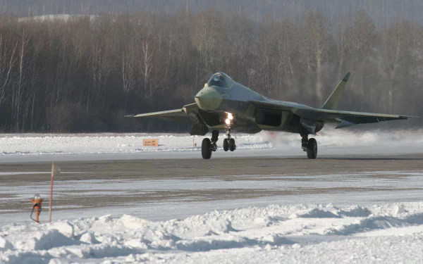 A Sukhoi Su-57 military aircraft takes off on a snowy runway, showcasing its sleek design against a backdrop of winter trees. High-definition desktop wallpaper.