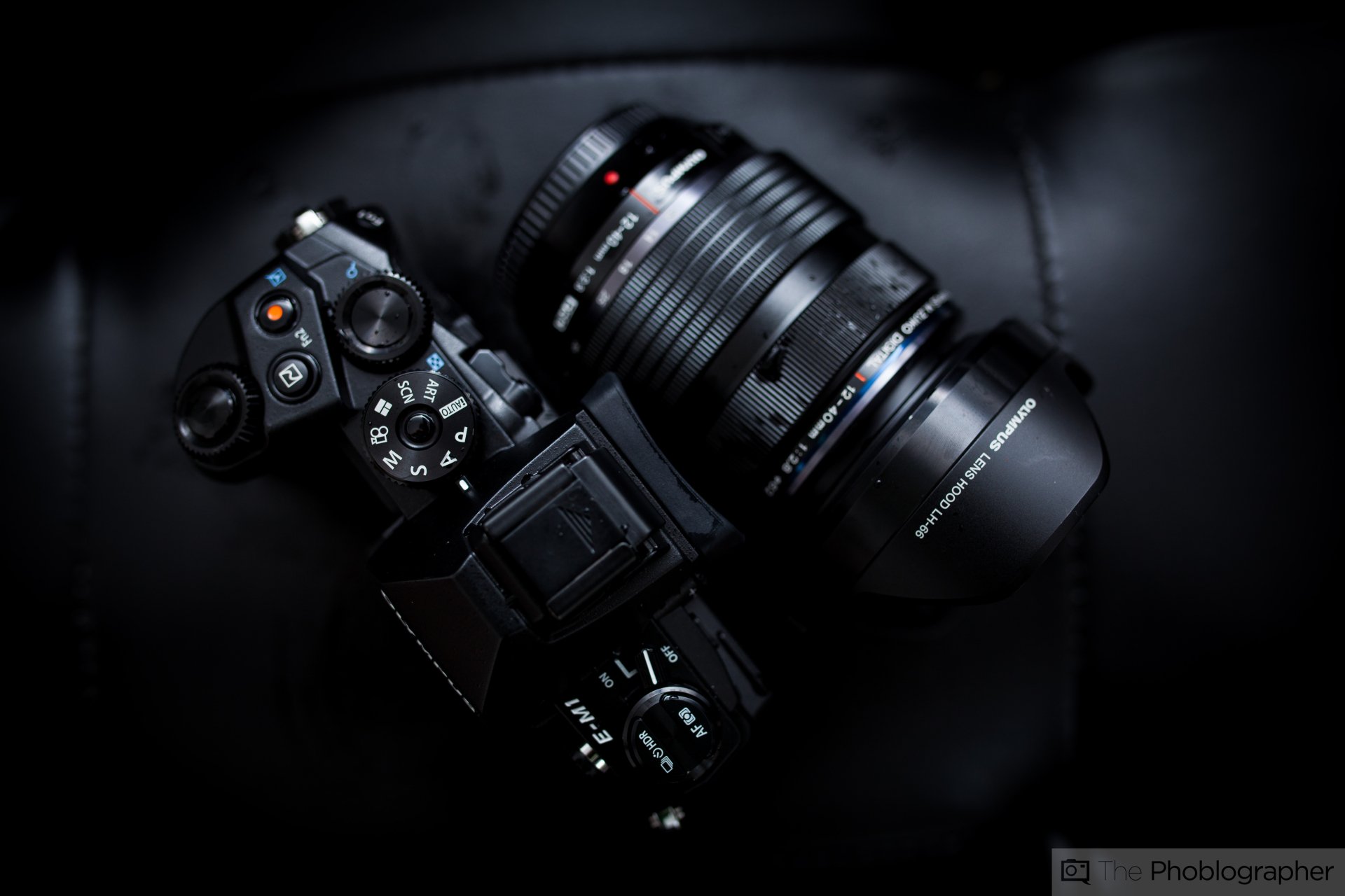 Close-up of an Olympus camera lens on a sleek, black camera, captured in high detail for a 4K Ultra HD PC desktop wallpaper background.
