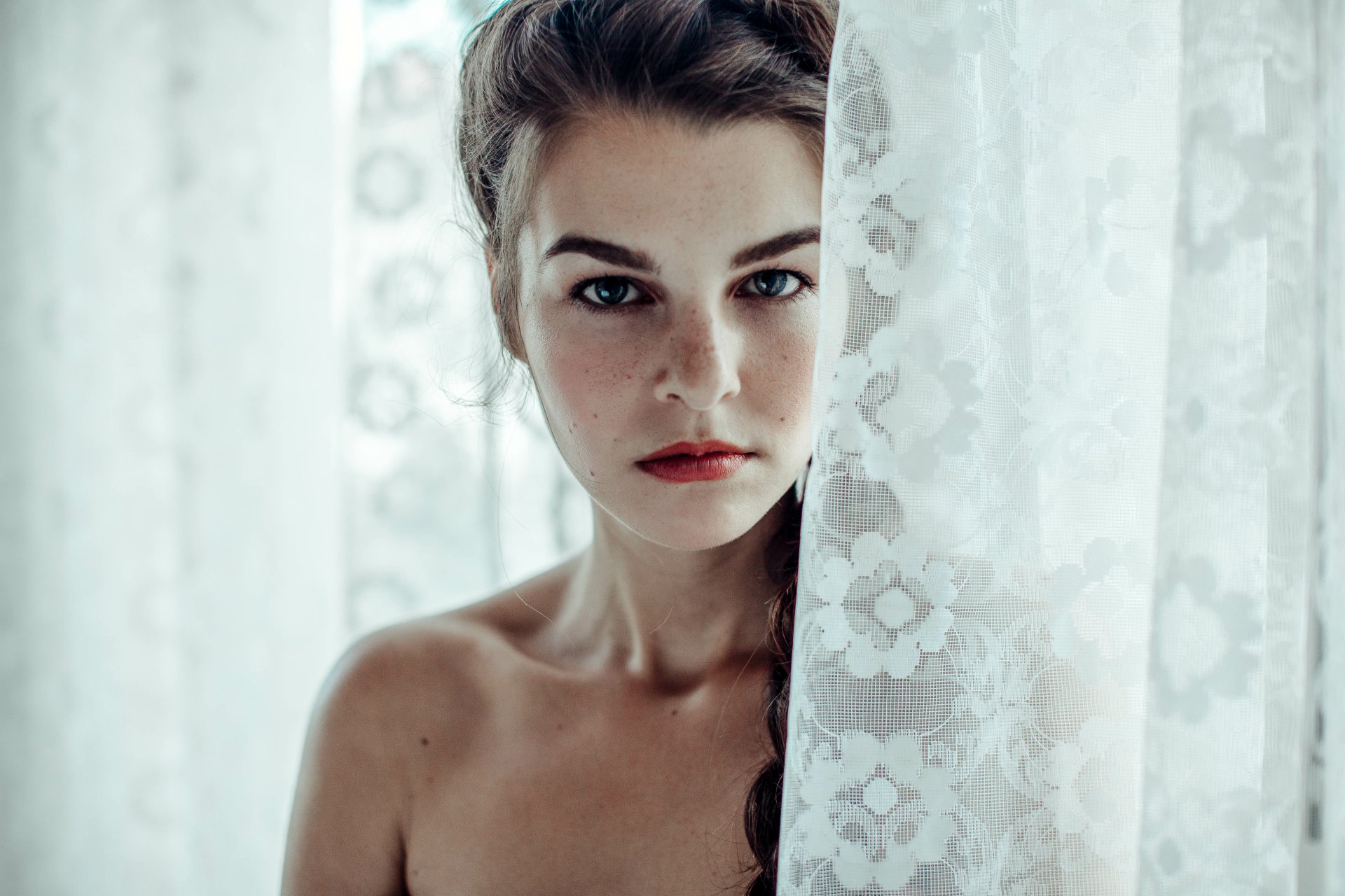 Portrait of a brunette woman with blue eyes and a braid, partially hidden behind sheer floral curtains, captured in 4K Ultra HD for a PC desktop wallpaper.