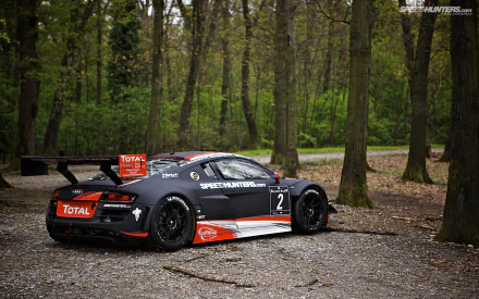 HD PC desktop wallpaper background: Audi R8 LMS race vehicle in black and red livery parked on a gravel path amid tall forest trees.