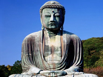 HD desktop wallpaper of a serene Buddha statue against a clear blue sky, surrounded by verdant greenery. The image evokes peace and embodies Buddhism's spiritual essence.