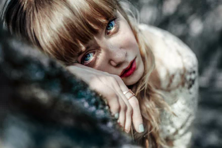 A blonde woman with striking blue eyes lies outdoors, her face softly illuminated in this 4K Ultra HD desktop wallpaper and background.