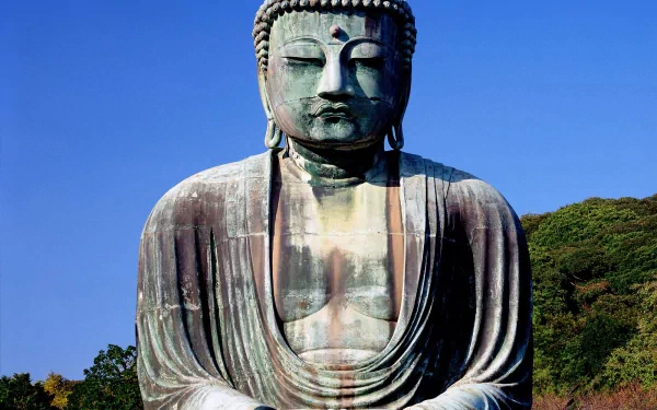 HD desktop wallpaper of a serene Buddha statue against a clear blue sky, surrounded by verdant greenery. The image evokes peace and embodies Buddhism's spiritual essence.