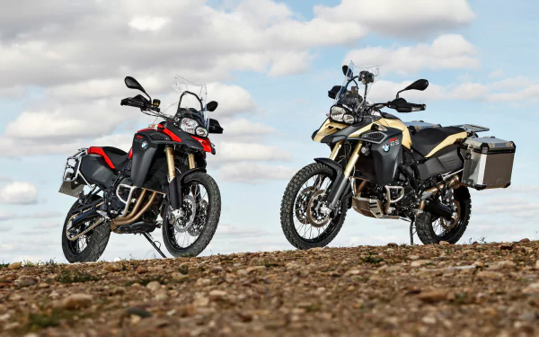 HD desktop wallpaper featuring two BMW F800GS Adventure motorcycles parked on rocky terrain beneath a cloudy sky.